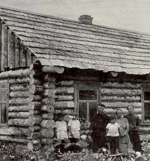 Eine Familie in der Verbannung vor einer Holzhütte, historisches Foto